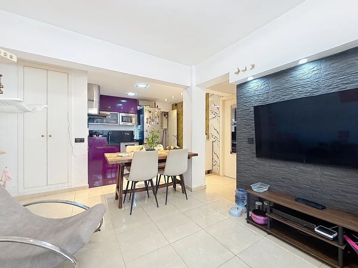 Open-plan lounge with wall-mounted television and kitchen beyond