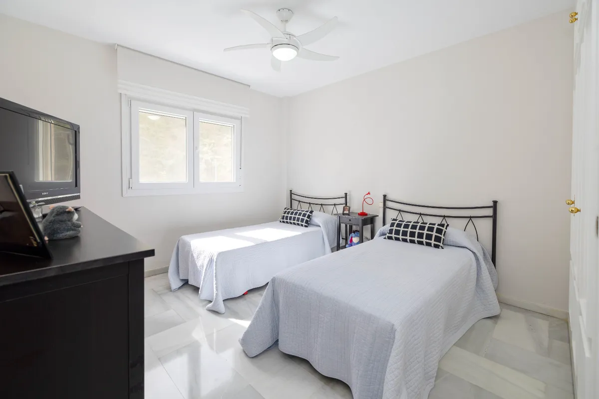 Twin bedroom with black metal beds and wide garden-facing window