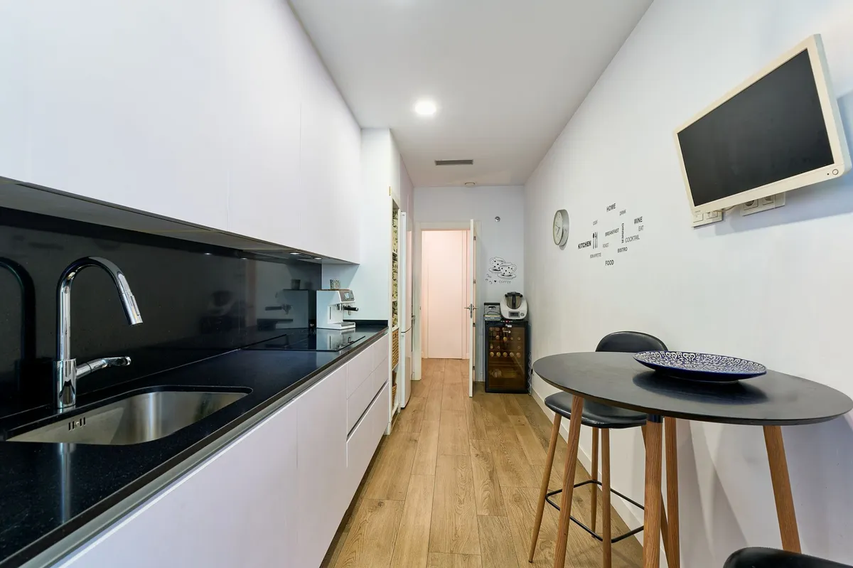 Streamlined kitchen with dark worktops and wall-mounted television
