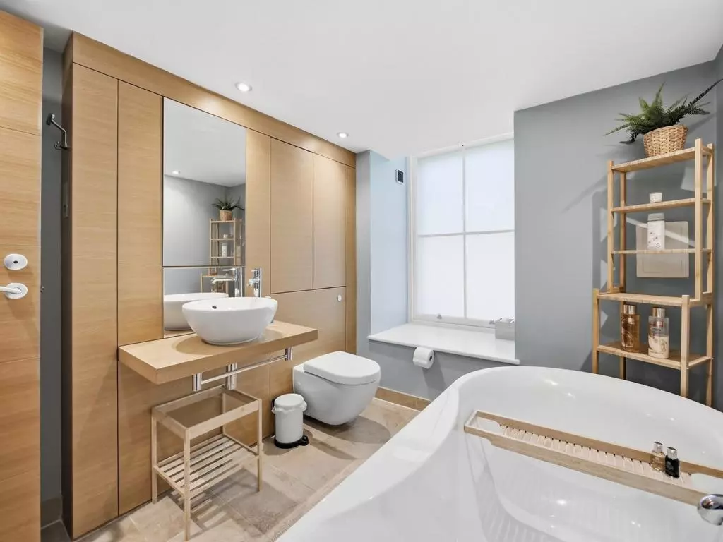 Spacious bathroom with bathtub, vanity and wood-panelled storage