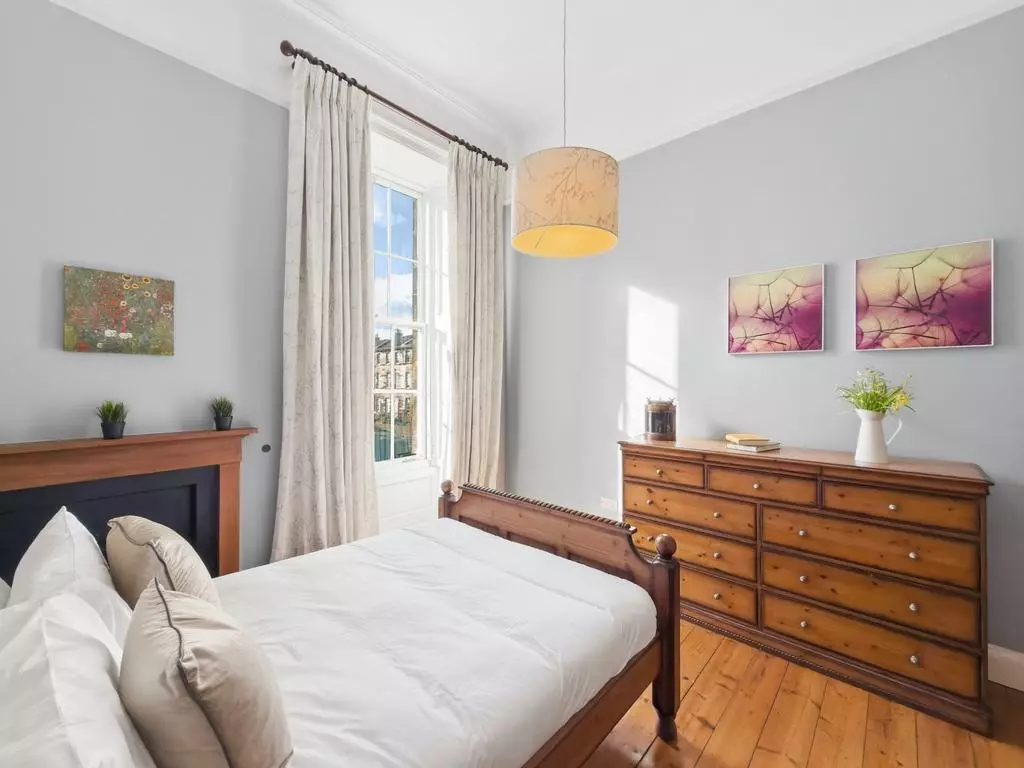 Bright double bedroom with tall window and traditional furniture