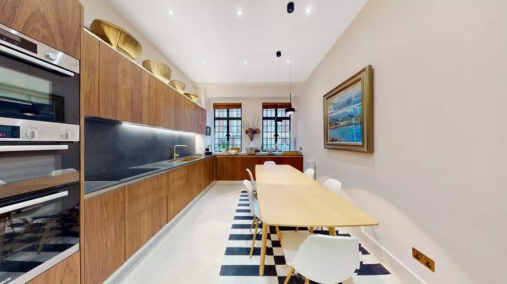 Long fitted kitchen with double oven, dark splashback and dining table